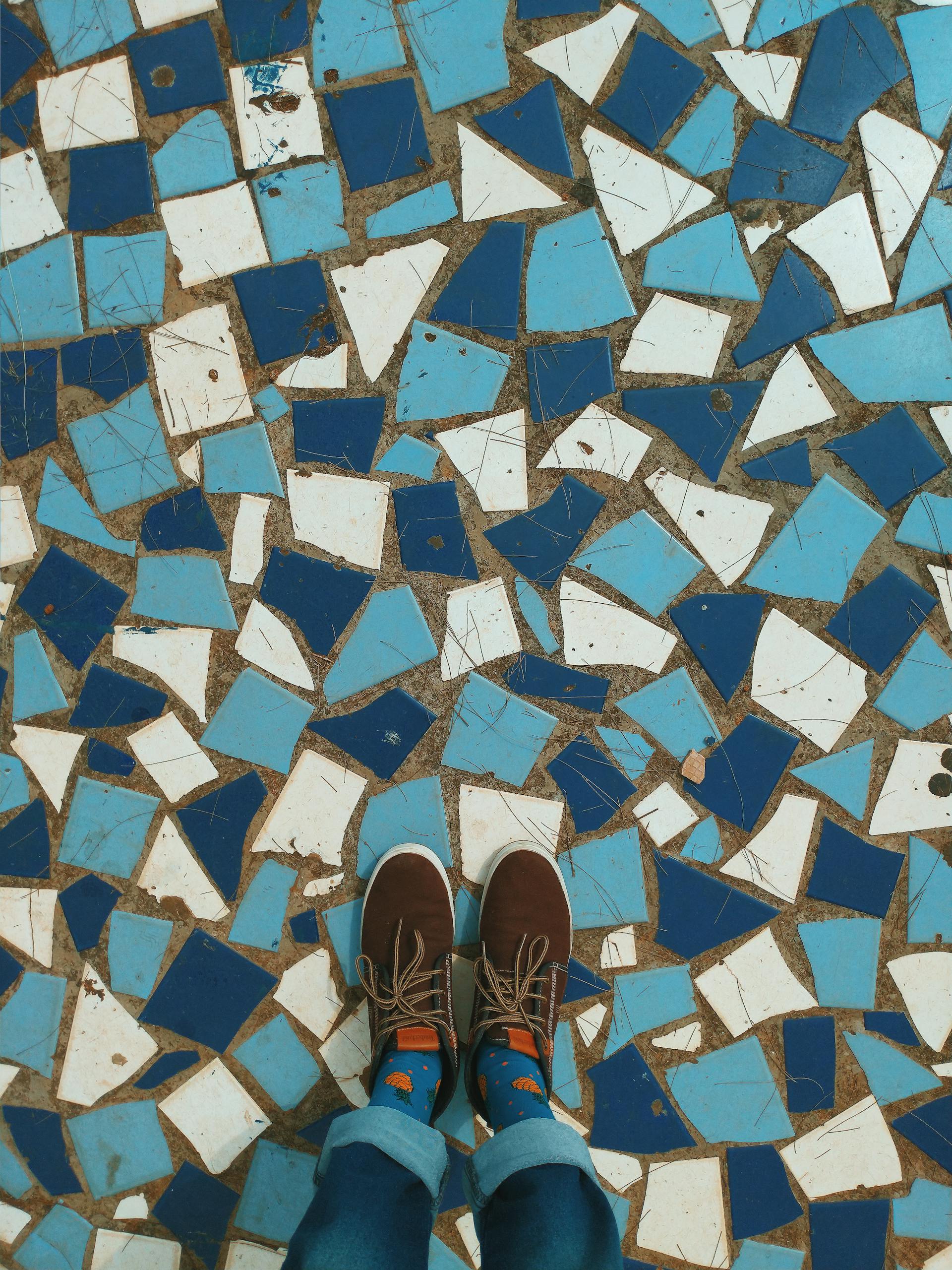 Top view of brown shoes on a vibrant blue and white mosaic tile floor.
